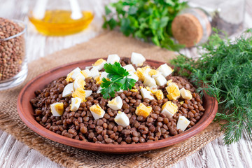 Boiled lentils with egg in ceramic bowls on a wooden background