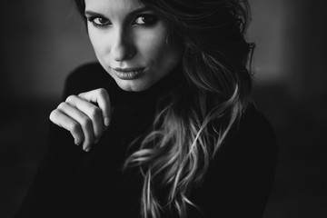 Beautiful woman with curls and full lips in a black turtleneck. Black and white art photo. Soft selective focus.