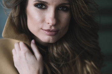 Beautiful sexy woman with curls and full lips in a beige coat in a loft style studio. Beauty and fashion. Soft selective focus.