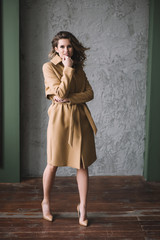 Beautiful sexy woman with curls and chubby lips and long legs in a beige coat in a loft style studio. Beauty and fashion. Soft selective focus.