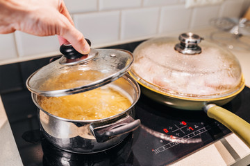 A man removes the lid from the pan - spaghetti in boiling water - home cooking in quarantine