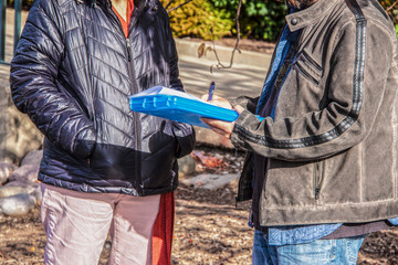 Survey taker talking to another person outdoors and writing answers on cold sunny day - cropped and...