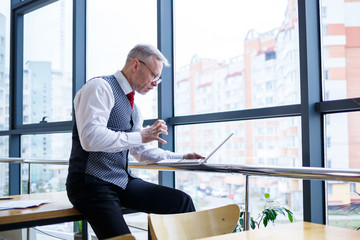 Adult male businessman, teacher, mentor working on a new project. Sits by a large window on the...