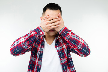 Asian guy in a checkered shirt wide open closes his eyes on an isolated white studio background
