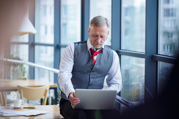 Adult male businessman, teacher, mentor working on a new project. Sits by a large window on the...