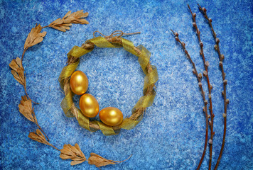 Easter wreath with golden eggsmin against blue background. Willow branches and ash seeds. Easter concept.