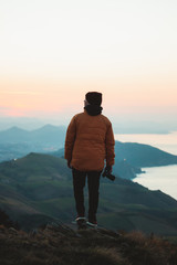 Fototapeta premium Young man wearing winter clothes holding a camera while watching the sunset