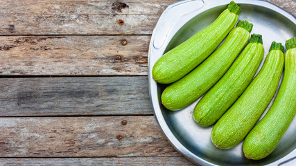 White zucchini lie on a steel vintage plate on wooden old boards background. View from above. Space for text.
