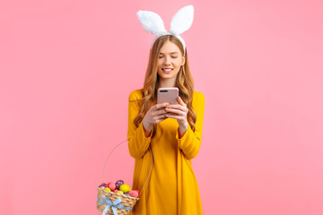 woman in the ears of an Easter Bunny, holding a basket of Easter eggs, with a mobile phone in her...