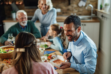 Happy man talking to his wife while passing her food at dining table.