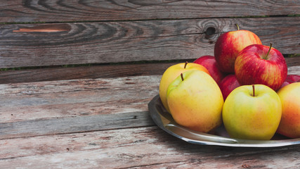 Red and yellow apples lie on a steel vintage plate on wooden old boards background.  Autumn harvest. Space for text.