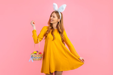 Obraz na płótnie Canvas Happy Easter. happy young woman wears rabbit ears on Easter day and holds a basket of Easter eggs, on an isolated pink background