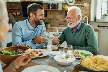 Happy senior man and his son toasting with wine at dining table.