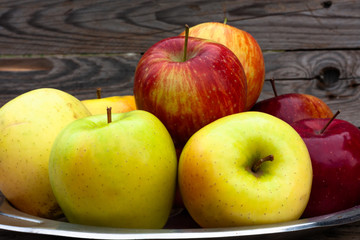 Red and yellow apples lie on a steel vintage plate on wooden old boards background.  Autumn harvest.
