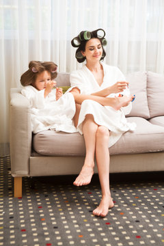 Mom and daughter  in white bathrobes with curlers in their hair Make manicure and pedicure at home. They have curlers in their hair. cheerful time together. chelter in place. stay home concept