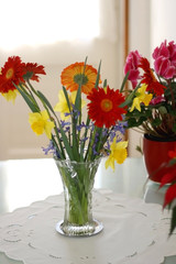 Crystal vase on a table with gerbera, hyacinth and daffodil flowers. Selective focus.