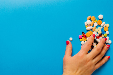 Female hand taking multi-colored pills lying on a blue background.
