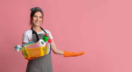 Smiling Young Woman Holding Basket With Cleaning Products And Pointing Aside