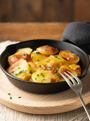 Roasted potatoes slices in iron skillet with herbs. Rustic background with copy space, close up.