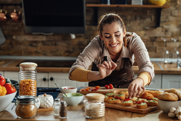 Happy woman enjoying while preparing bruschetta in the kitchen.