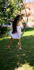 A joy moment of  young girl with a white dress and long hair, she is  jumping of a swing in a garden in spring