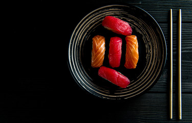 salmon and tuna sushi on a black plate and a black wooden background