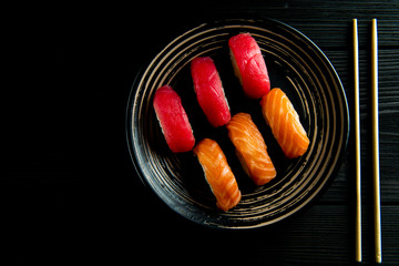 salmon and tuna sushi on a black plate and a black wooden background