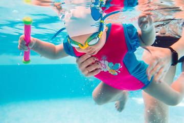 A swimming teacher teaches a kid to swim in the pool.