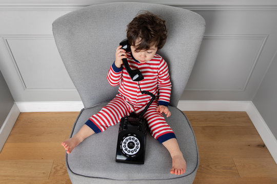 Overhead view of toddler sitting on a chair talking on vintage phone