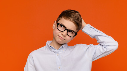 Doubtful teenage boy in glasses scratching his head