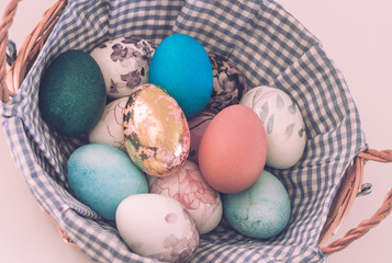 Wicker basket with colored Easter eggs on a light background, close-up