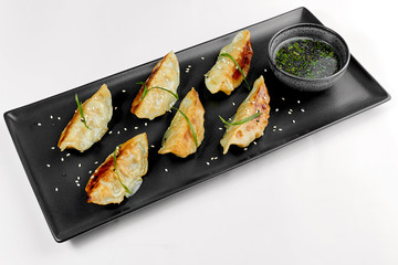 Japanese gyoza dumplings on a black plate with sauce on a white background