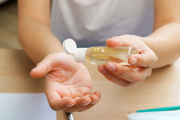 Young man applying sanitizer gel on his hands while sitting at his working table in office