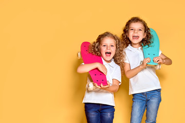 Two Active and happy girls with curly hair having fun with penny board, smiling face stand skateboard. Penny board cute skateboard for girls. Lets ride. Girl with penny board yellow background.