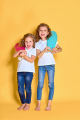 Two Active and happy girls with curly hair having fun with penny board, smiling face stand skateboard. Penny board cute skateboard for girls. Lets ride. Girl with penny board yellow background.