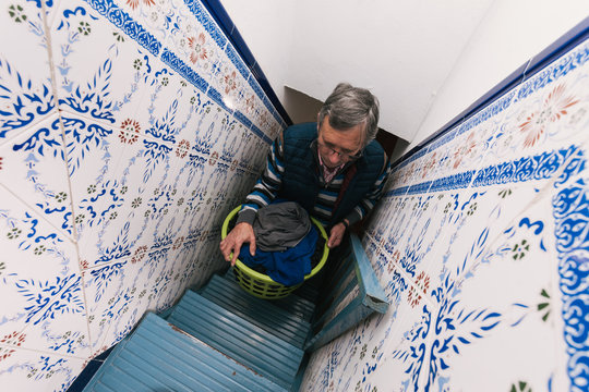 Older Man Taking Clothes Up To The Terrace Up The Stairs To Hang Them After Doing The Laundry. Homework. Househusband. Selective Focus.