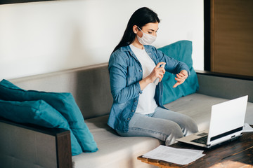 Health care and hygiene. Woman in face mask spreading sanitizer on hands before touching laptop. Infection diseases prevention