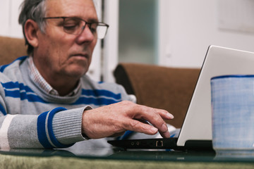 Senior man using a computer at home. Telecommuting during quarantine. Communication with family members during confinement. Selective focus.