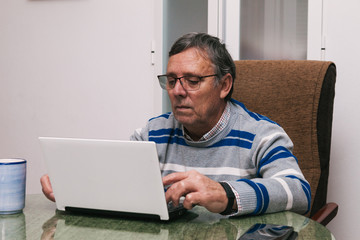 Senior man using a computer at home. Telecommuting during quarantine. Communication with family members during confinement. Selective focus.