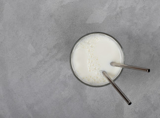 Milk in a glass with a metal tube on a light gray background top view