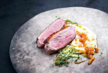 Traditional gourmet duck breast filet with mashed potatoes and orange sauce as closeup on a rustic modern design plate left