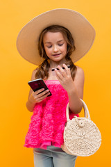 young tourist girl in a summer pink t-shirt with a straw hat on her head chatting on the phone on a yellow studio background