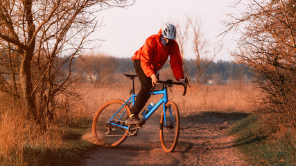 A cyclist on a gravel bike rides along the road raising dust from the rear wheel at sunset. Gravel...