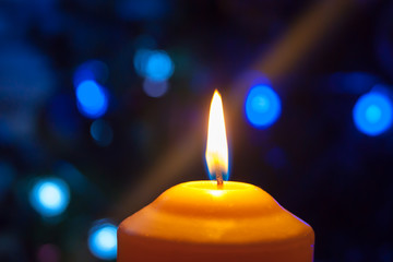 A burning orange candle on a dark background with blue lights - a Christmas New Year's eve divination mystic esoteric romance love mood. Horizontal photo, side, focus or defocus