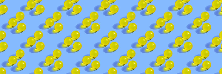 Round yellow pills on blue background. Seamless pattern with gelatin capsule. Horizontal banner, site header. Pharmacy health care concept. Organic liquid nutrition, oil, vitamin, beauty supplement.