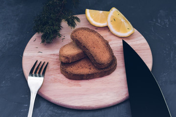 dry toasted bread with sauce, seasonings and lemon against a dark gray stone background, with a knife and fork. Rusks