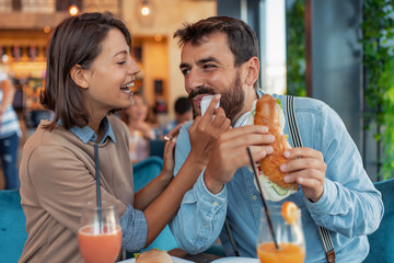 Beautiful young couple eating sandwiches and smiling