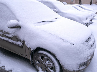 Cars in the parking lot are covered with freshly fallen snow.