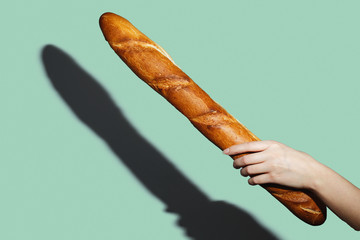 Female hands hold a bread loaf on green background. Flat lay, direct light.
