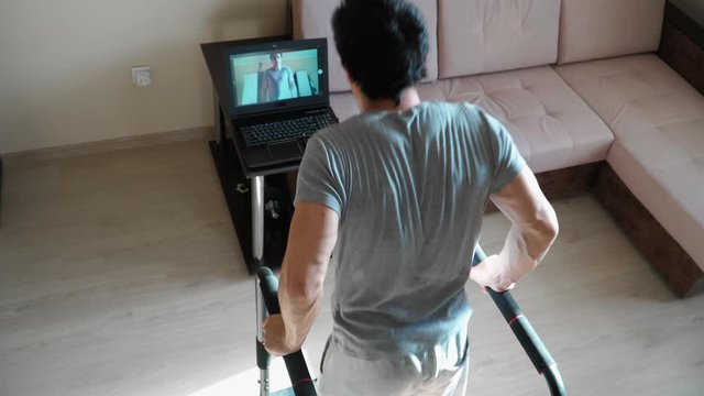 A young man conducts online training at home. Shows exercise dips shooting for web camera of the laptop. Remote work during the quarantine. Top view